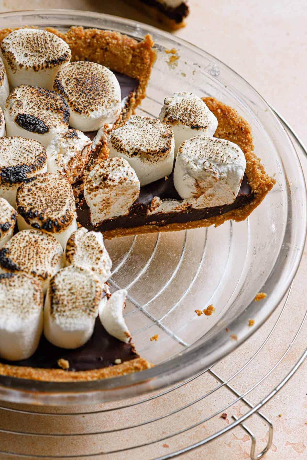 A glass pie plate with a s'mores pie slice from the side to show the layers of the pie.