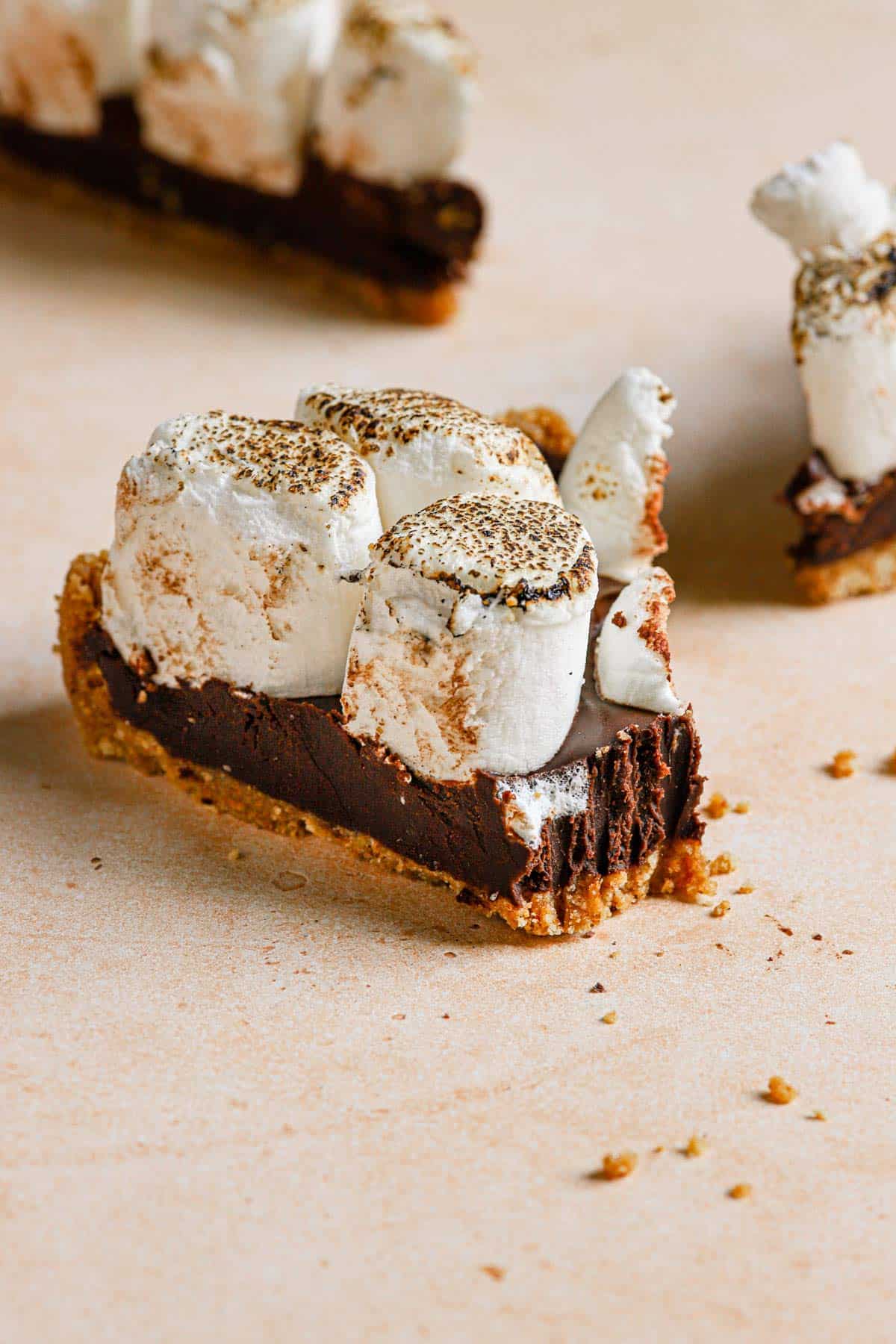 A slice of no-bake s'mores pie on a counter with a bite take out and more slices in the back.