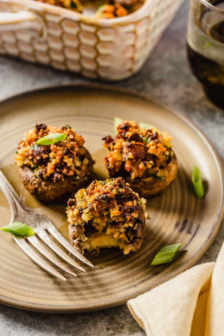A small plate with three sausage stuffed mushrooms and a fork on the left side of the plate with the front mushroom missing a bite.