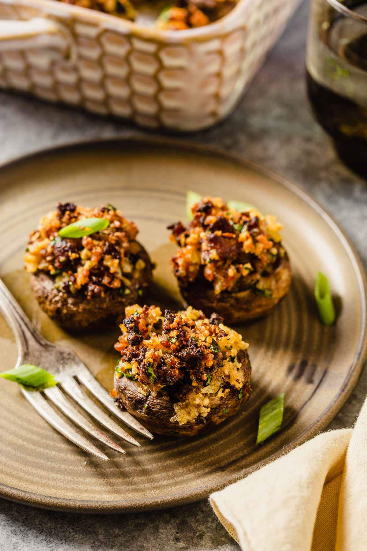 A small plate with a fork and three sausage stuffed mushrooms with green onion on the plate.