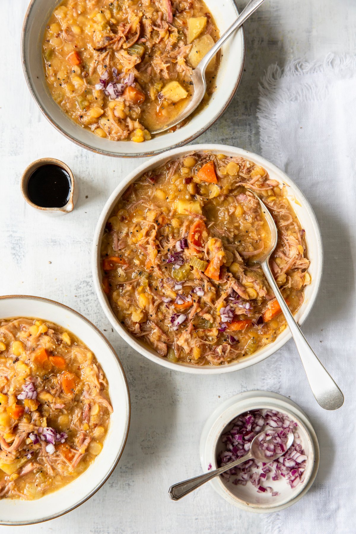 Three bowls of Ham and Split Pea Soup with bowls of chopped onions and balsamic vinegar