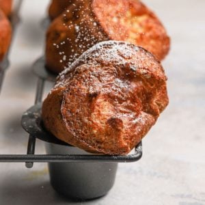 Golden brown baked breakfast popovers in a grey popover baking pan dusted with powdered sugar