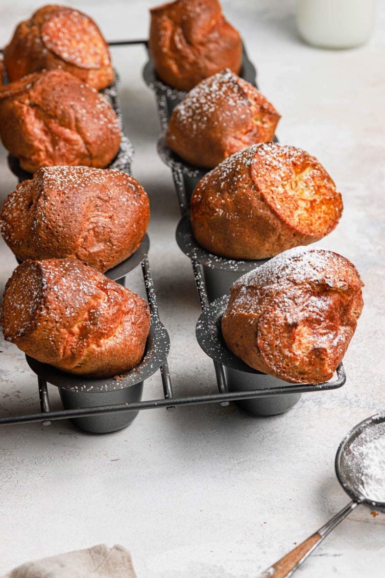Golden brown baked breakfast popovers in a grey popover baking pan dusted with powdered sugar