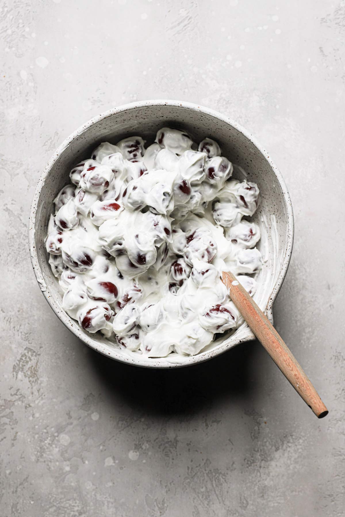 An overhead view of the author mixing the whole seedless grapes with the homemade cream cheese dressing with a rubber spatula for this grape salad recipe