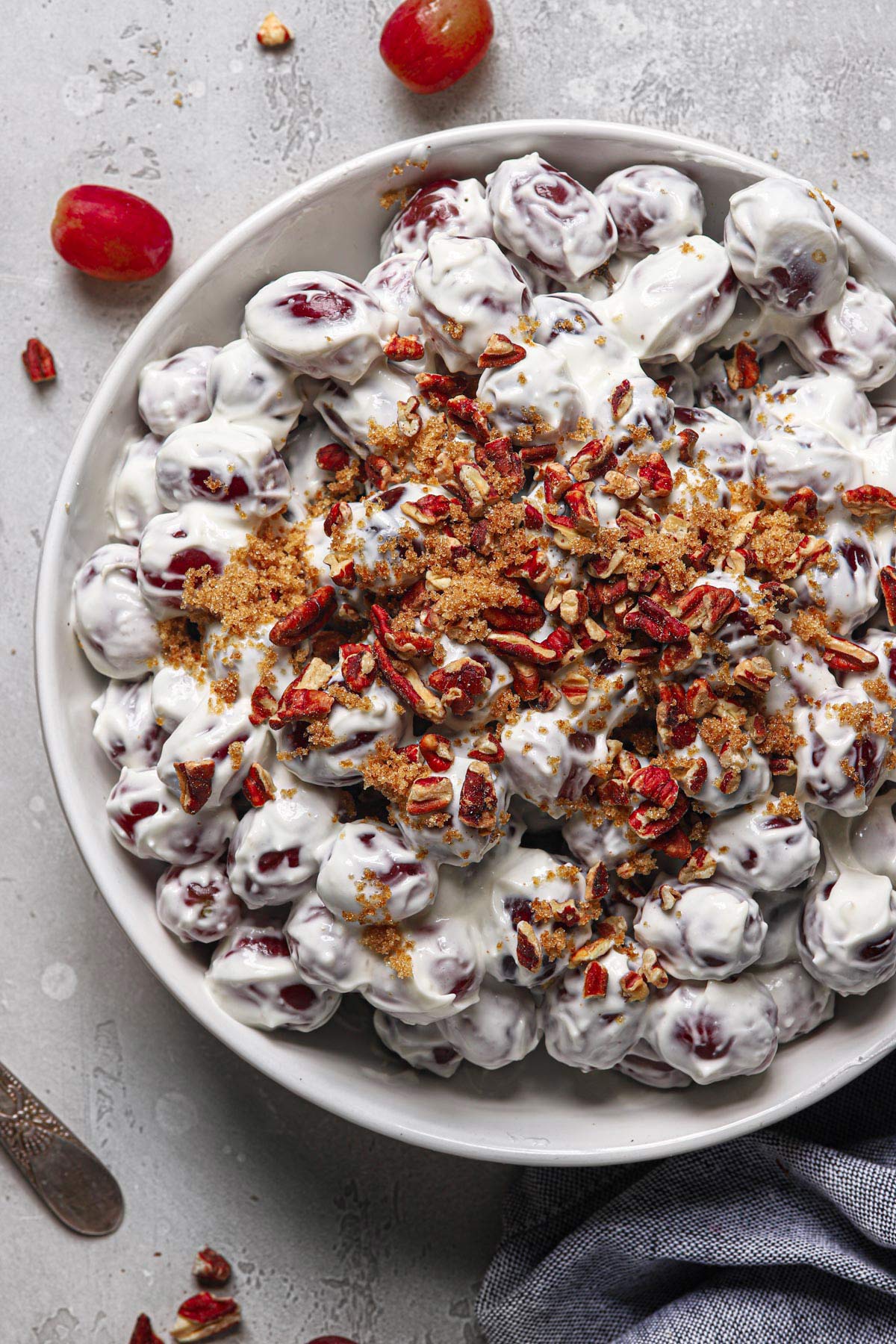 a large white serving bowl filled with this homemade grape salad recipe topped with brown sugar and chopped toasted pecans