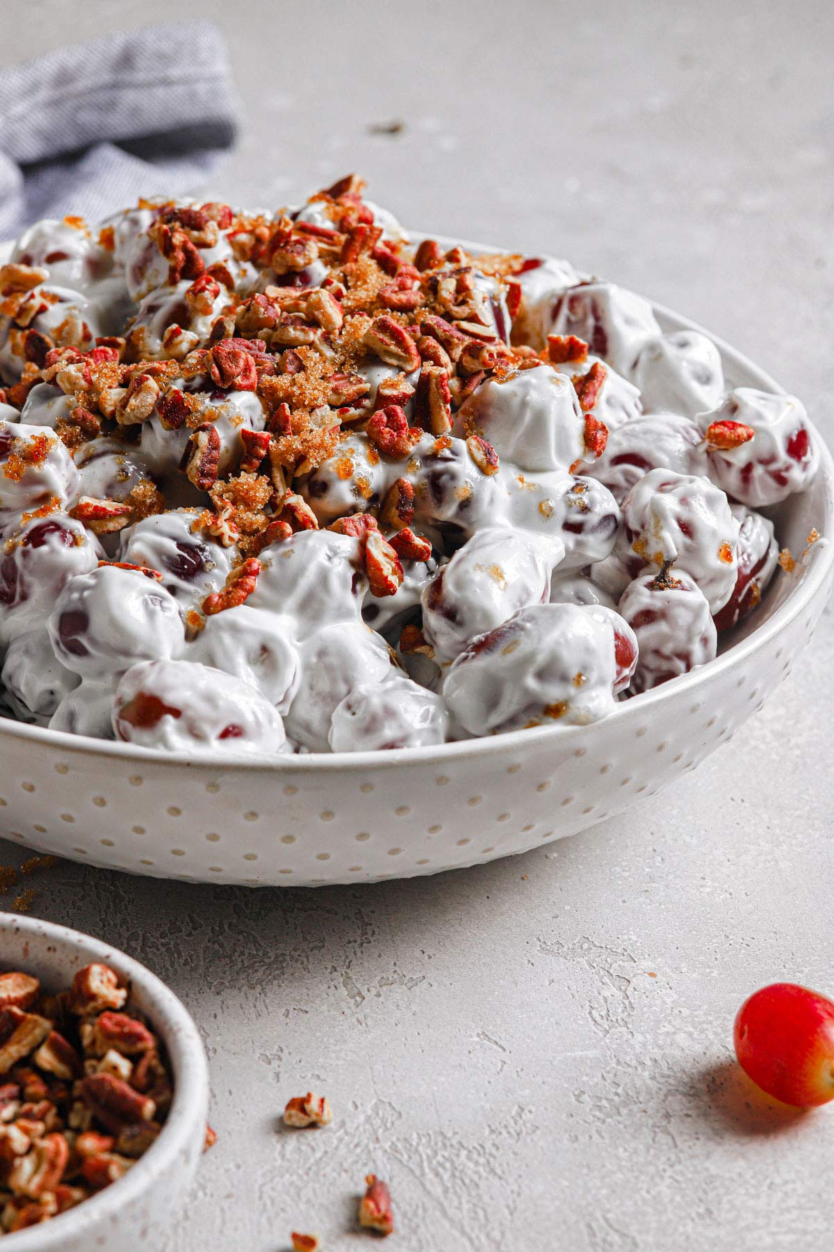 side view of a large white serving bowl filled with this homemade grape salad recipe topped with brown sugar and chopped toasted pecans