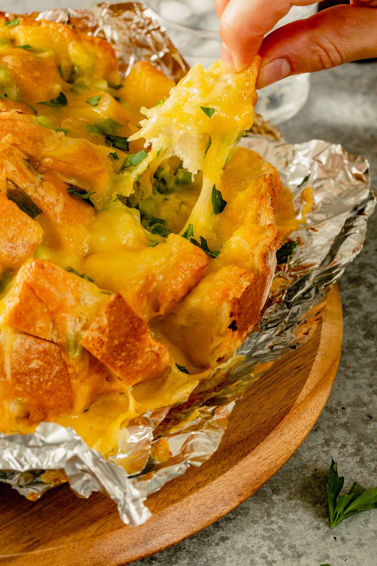 A piece of pull-apart bread being pulled off with melted cheese hanging off.