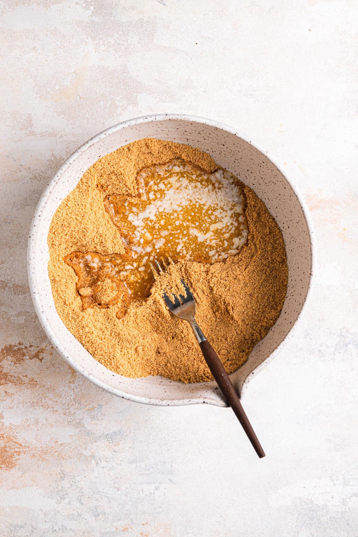 Melted butter added to bowl with graham cracker crumbs, brown sugar, and salt.
