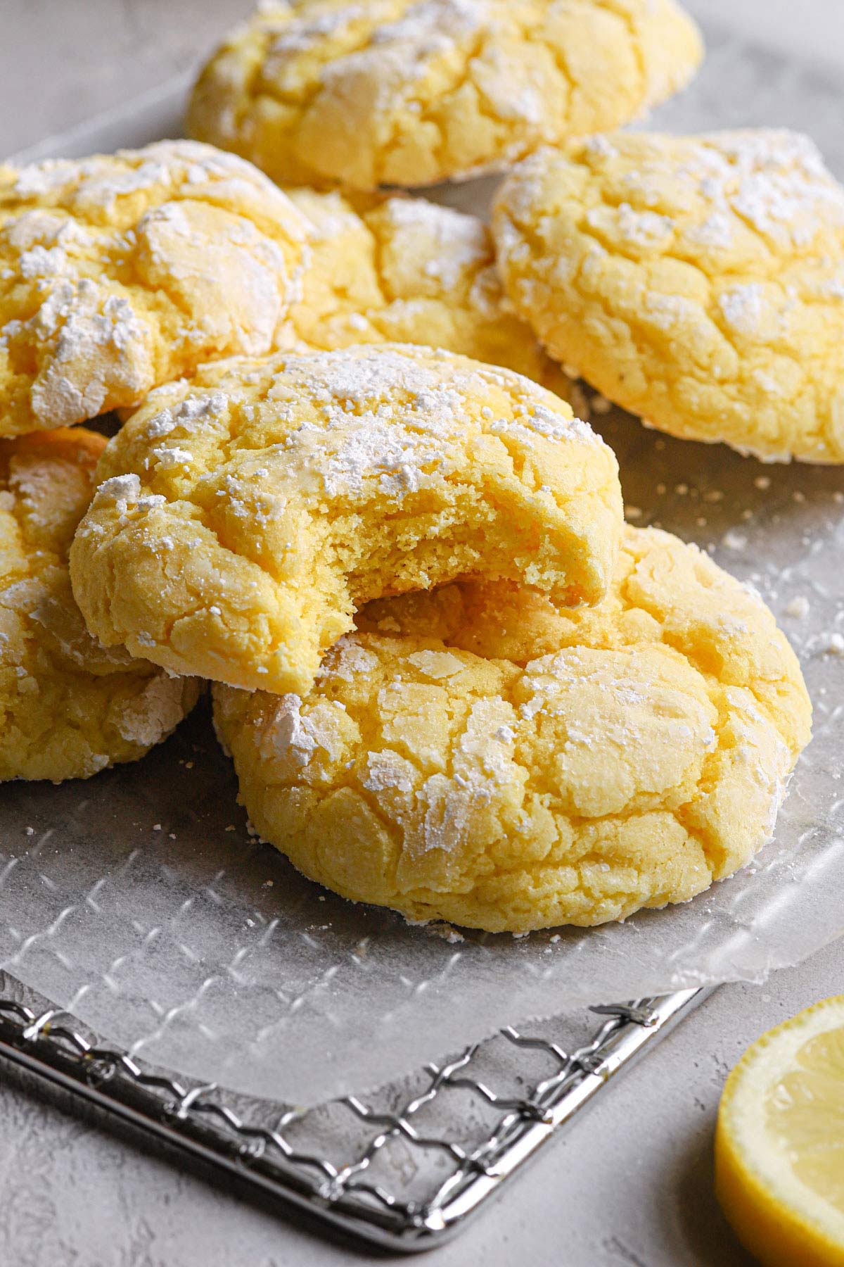 a few lemon crinkle cookies resting on a wire cooling rack with a bite taken out of the cookie in the forefront