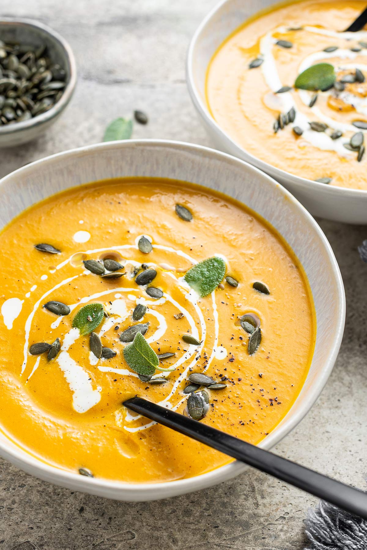 Bowl of pumpkin soup garnished with pumpkin seeds and sage leaves.