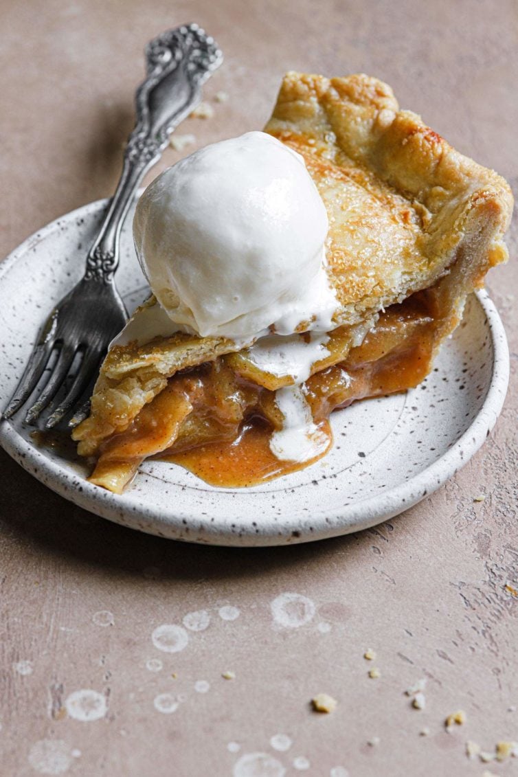 a slice of this salted caramel apple pie served on a stoneware plate with vanilla ice cream