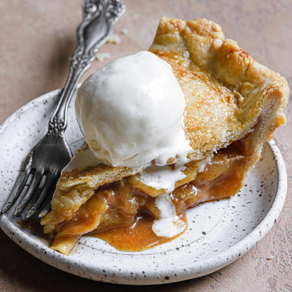 a slice of this salted caramel apple pie served on a stoneware plate with vanilla ice cream
