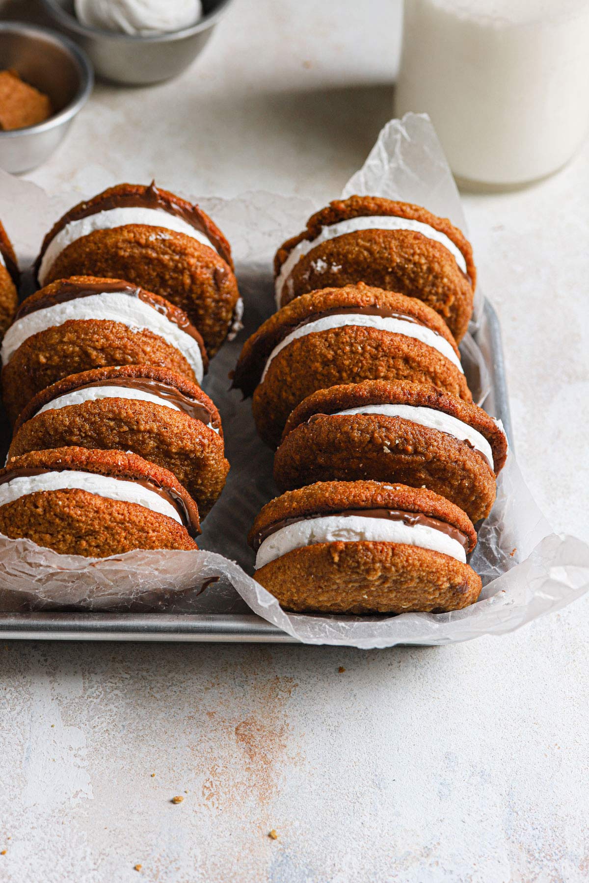 S'mores whoopie pies on silver serving tray with bottle of milk in background.
