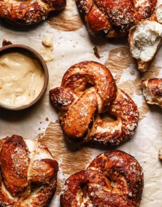 homemade soft pretzels on a baking tray garniched with coarse salt and with a beer cheese dipping sauce on the side