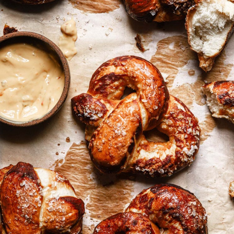 homemade soft pretzels on a baking tray garniched with coarse salt and with a beer cheese dipping sauce on the side