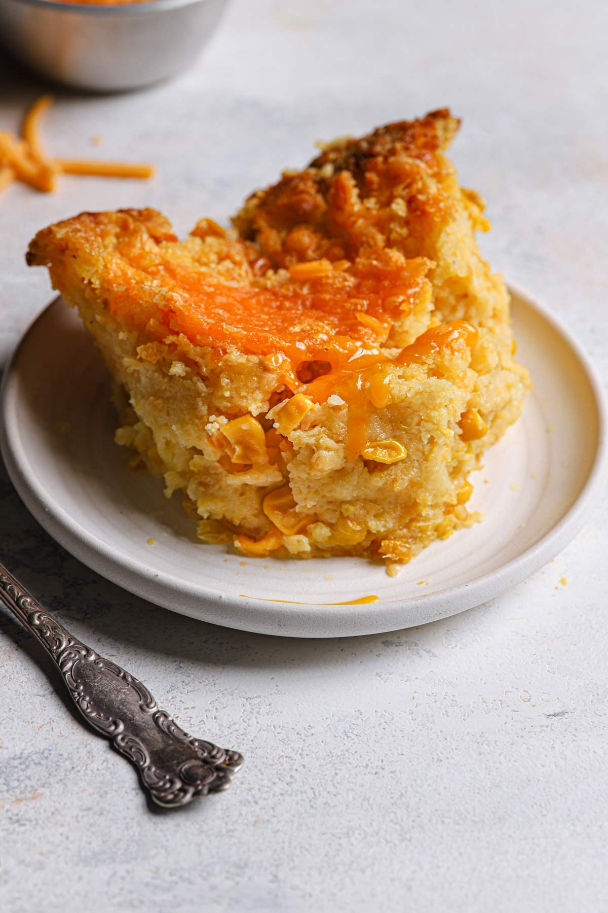 A serving of cheesy creamed corn casserole on a round plate.