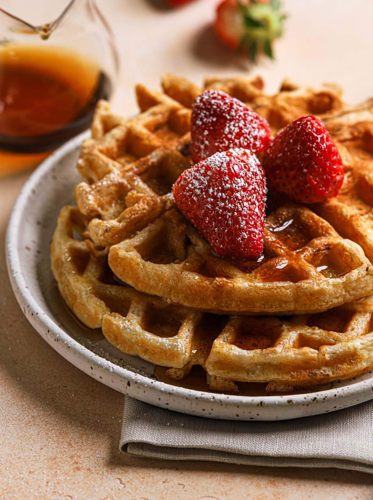 Two Belgian waffles on a plate with strawberries and powdered sugar on top.