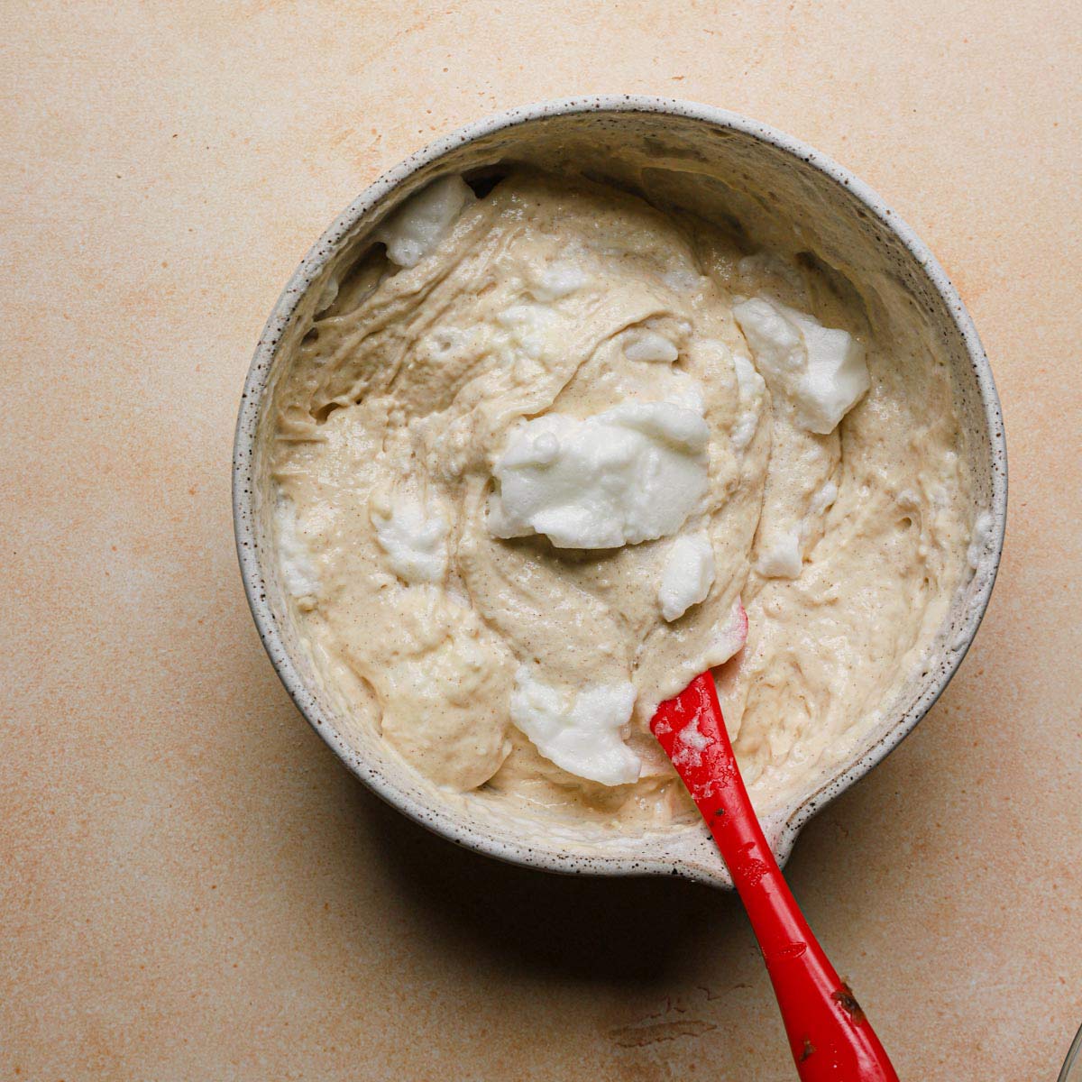 Egg whites being folded into waffle batter with a red rubber spatula.