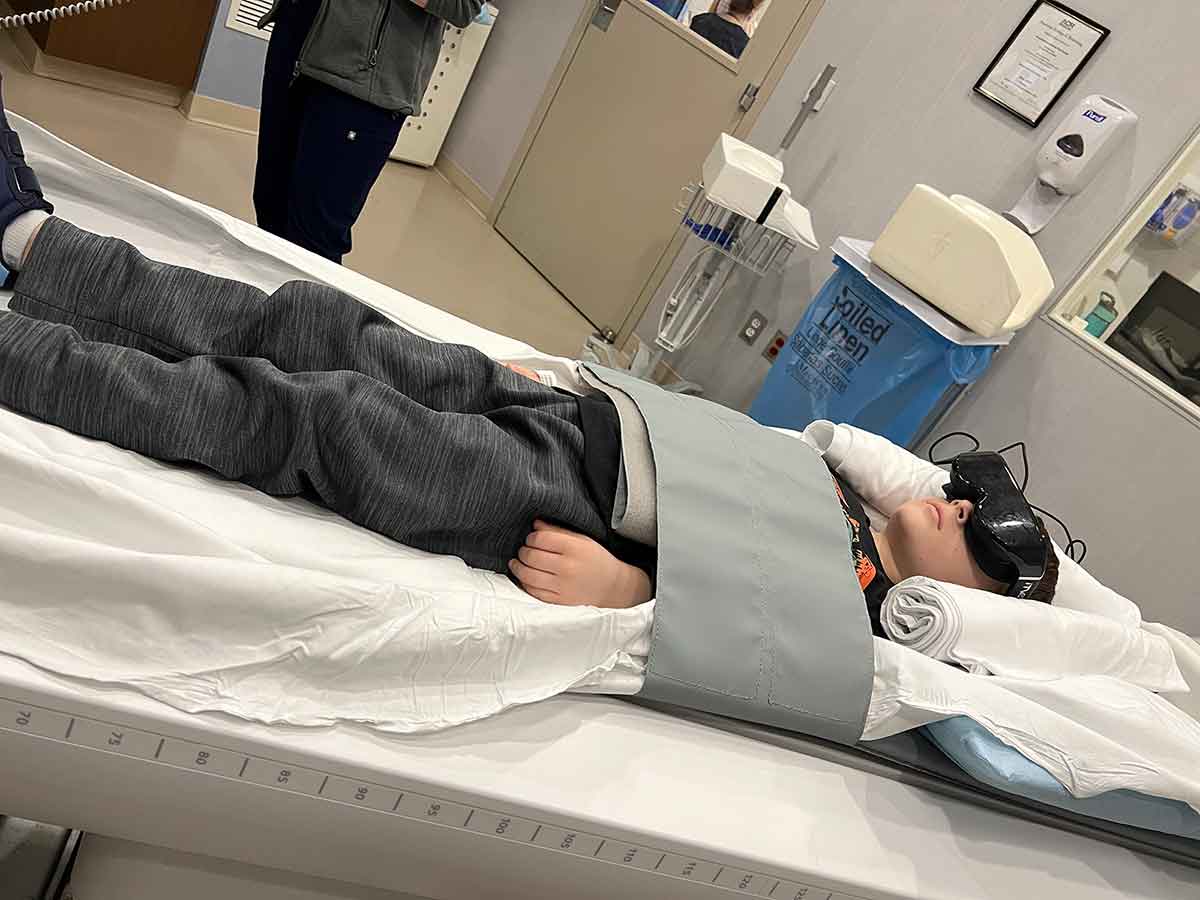 Boy laying on scan table wearing black movie goggles.