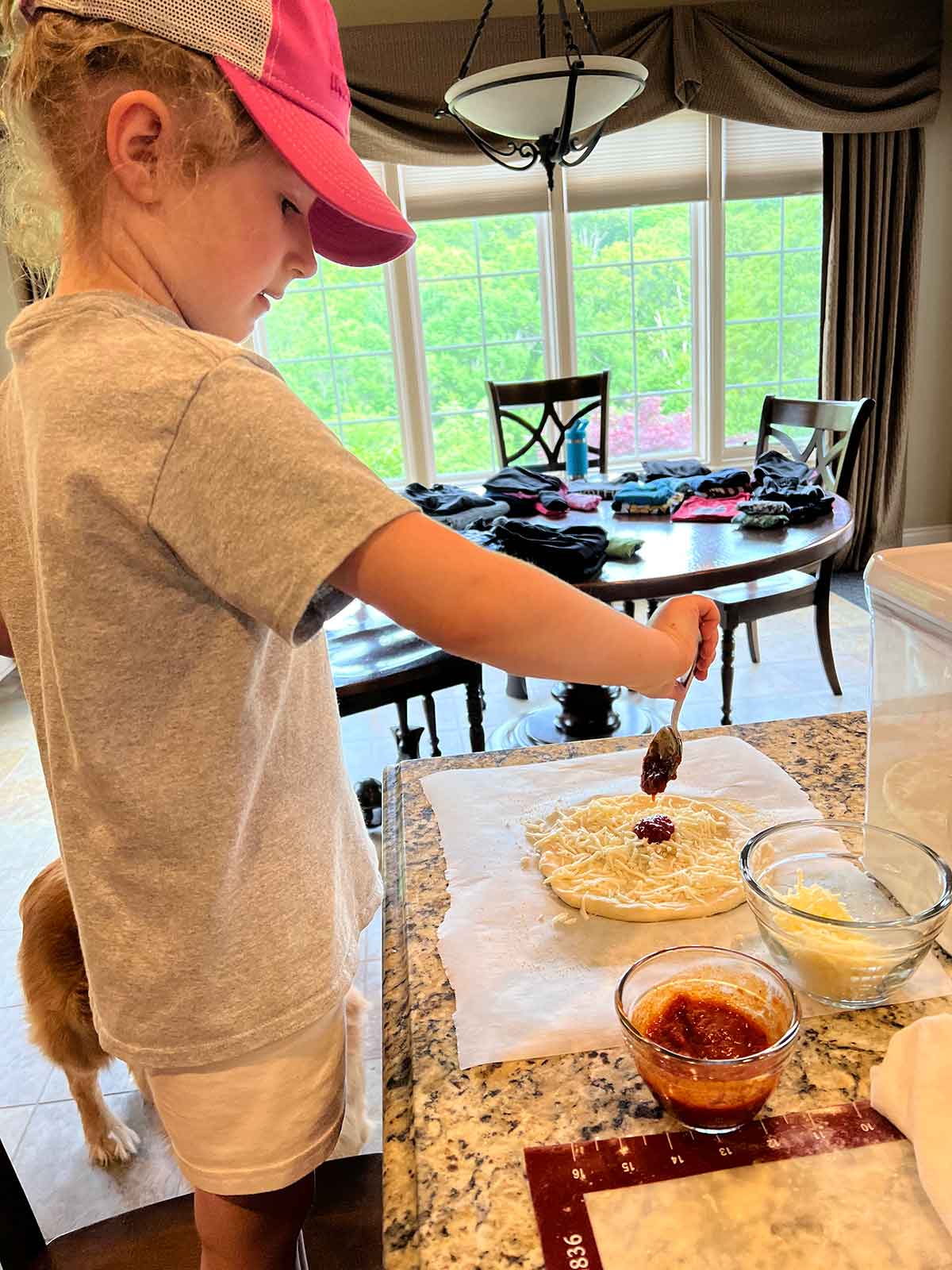 Girl spooning sauce on pizza crust.