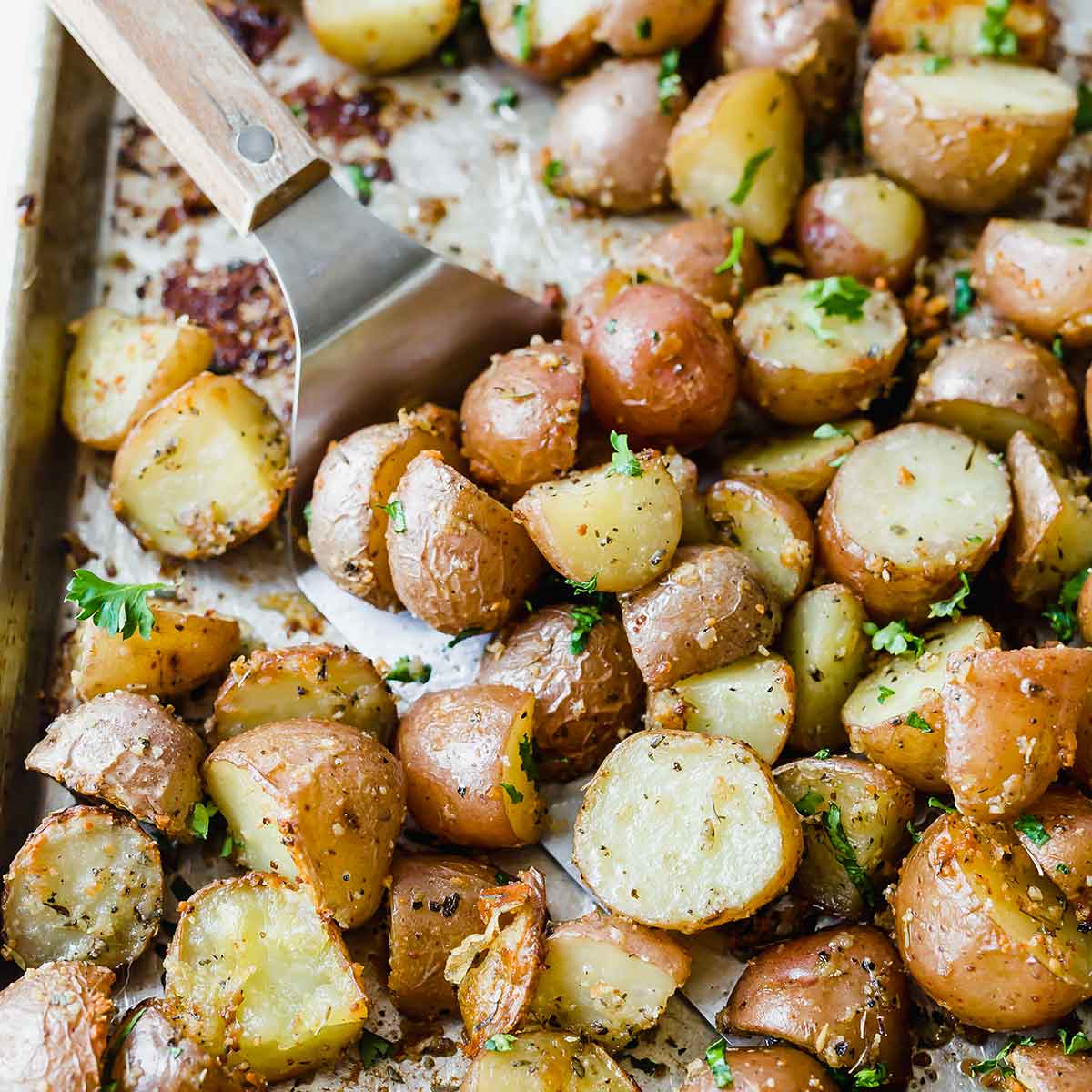 Silver spatula sliding underneath roasted potatoes on a baking sheet.