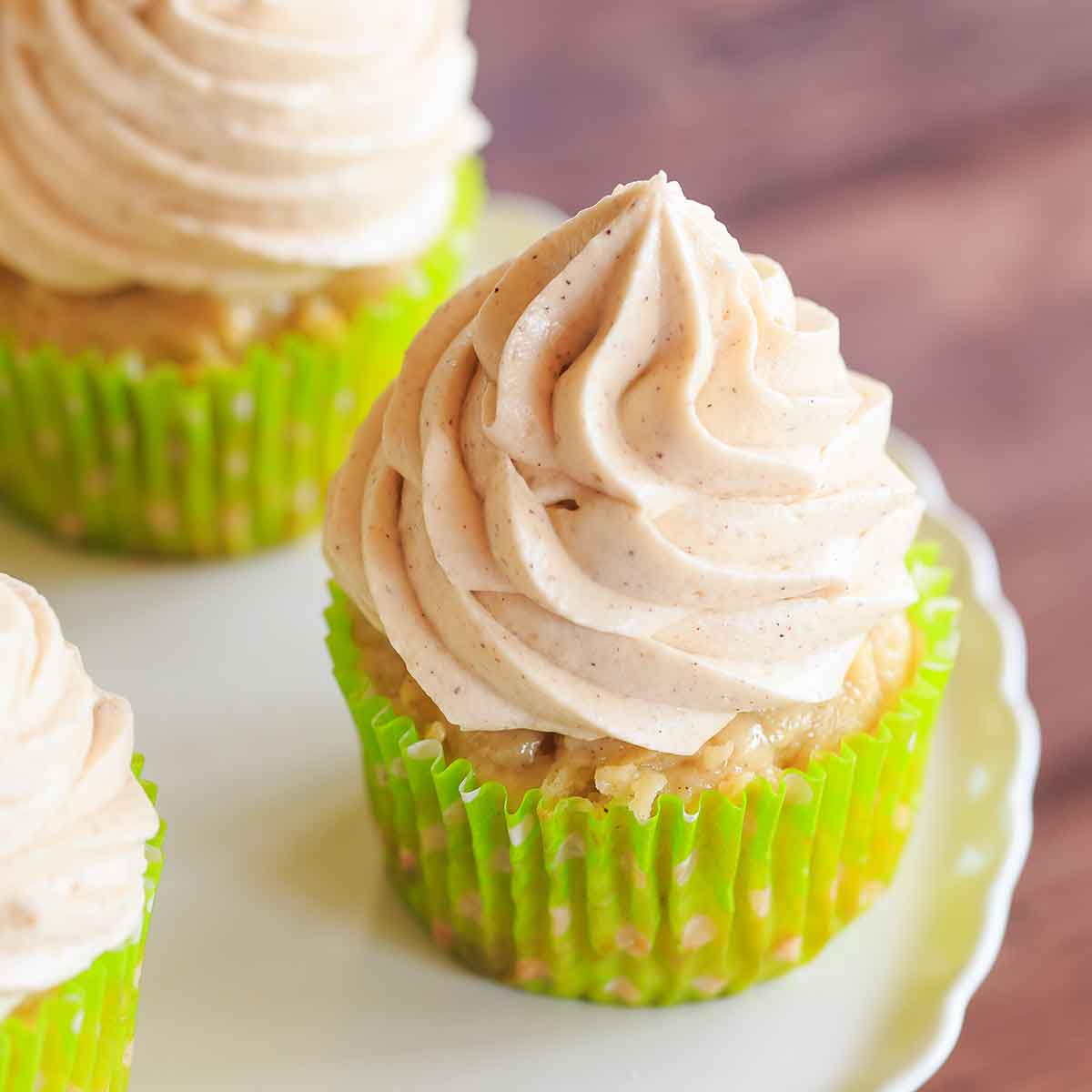 Apple cupcake with a green liner and swirls of cinnamon cream cheese frosting on top.