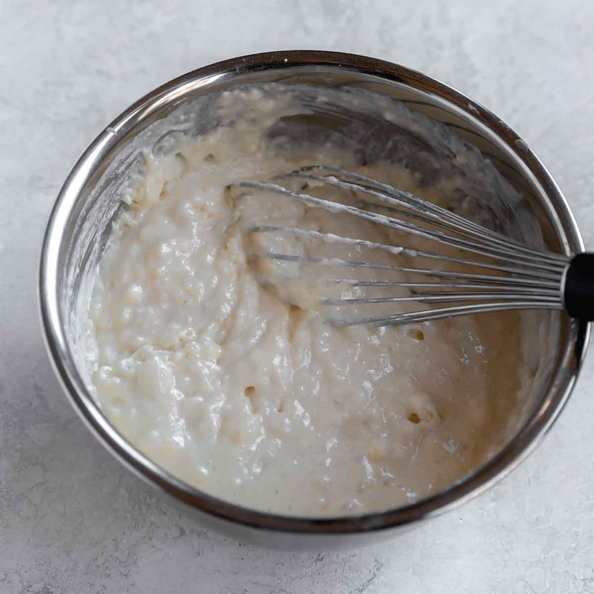 Waffle batter in a stainless steel bowl with a whisk in the batter.