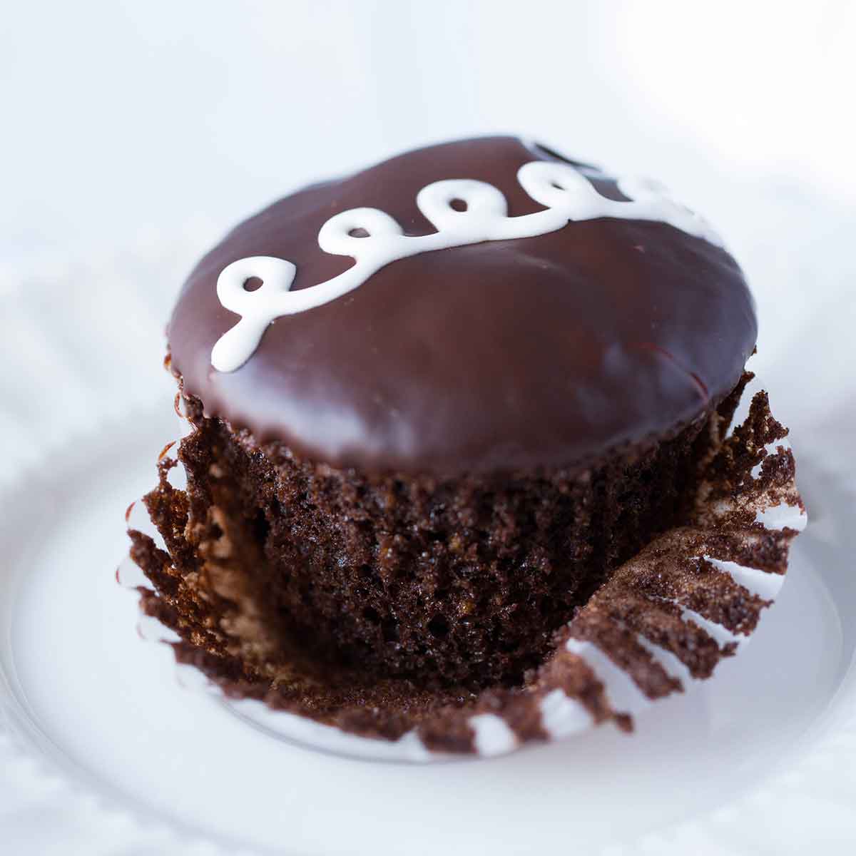 Chocolate cupcake with liner partially removed and white swirls iced across the top.