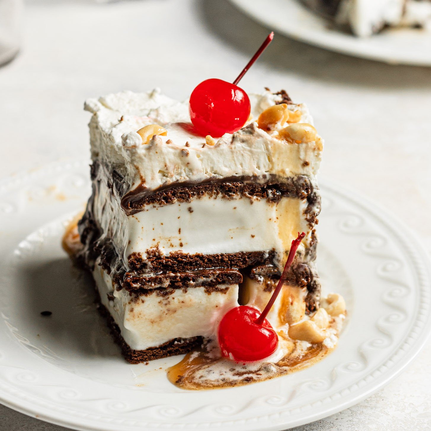 Square slice of ice cream sandwich cake on white plate with extra cherry on the side.