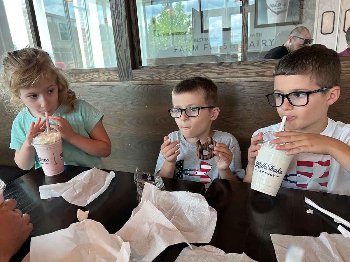 One girl and two boys drinking milkshakes.