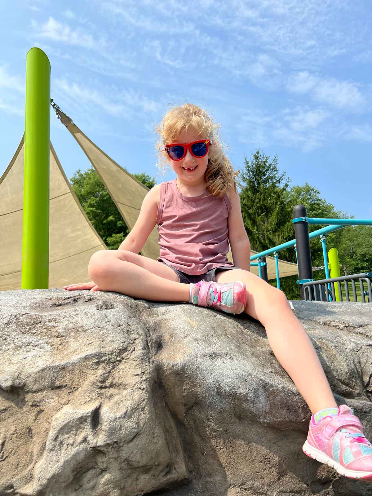 Girl sitting on top of a rock structure at a playground.