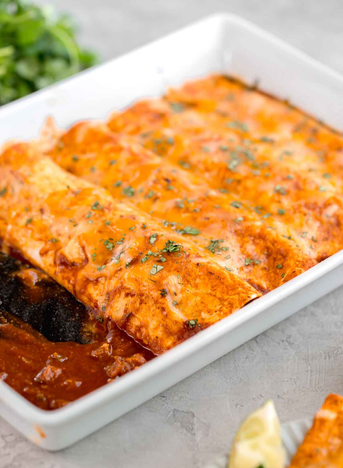 Baked enchiladas in baking dish with pool of enchilada sauce in bottom.