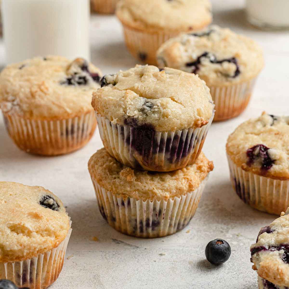 Blueberry muffins on a counter, two of them stacked on top of each other.