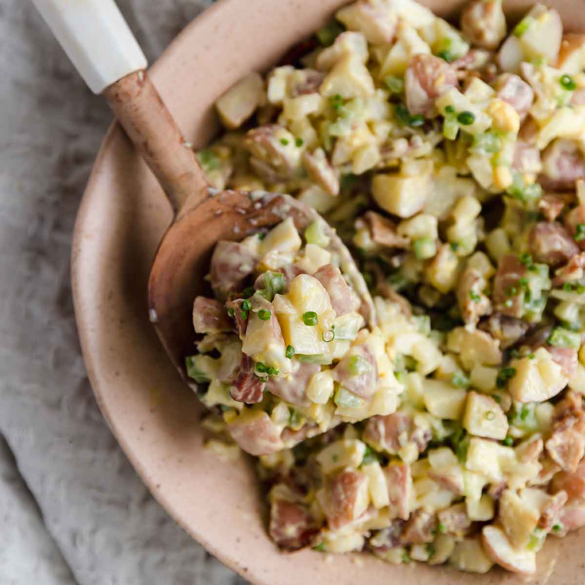 Close up photo of a scoop of potato salad on a wooden serving spoon.