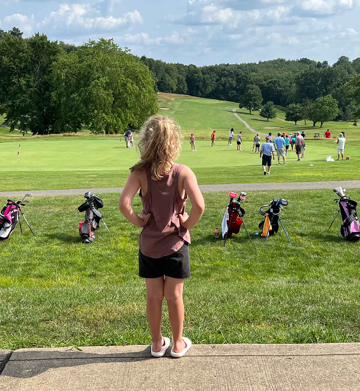 Girl standing with hands on hips in front of a practice putting green.