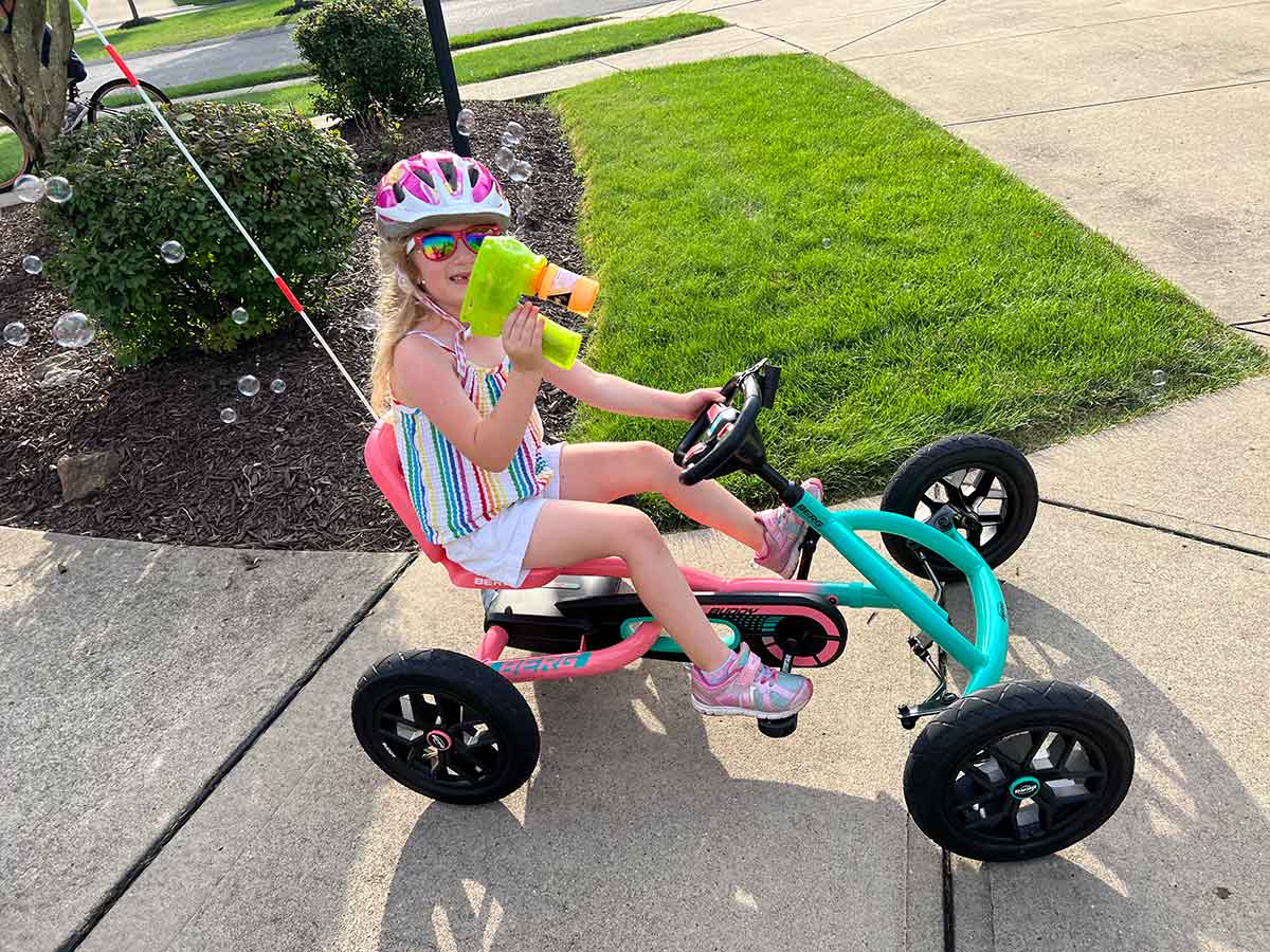 Girl riding a go kart bike while using a bubble machine.
