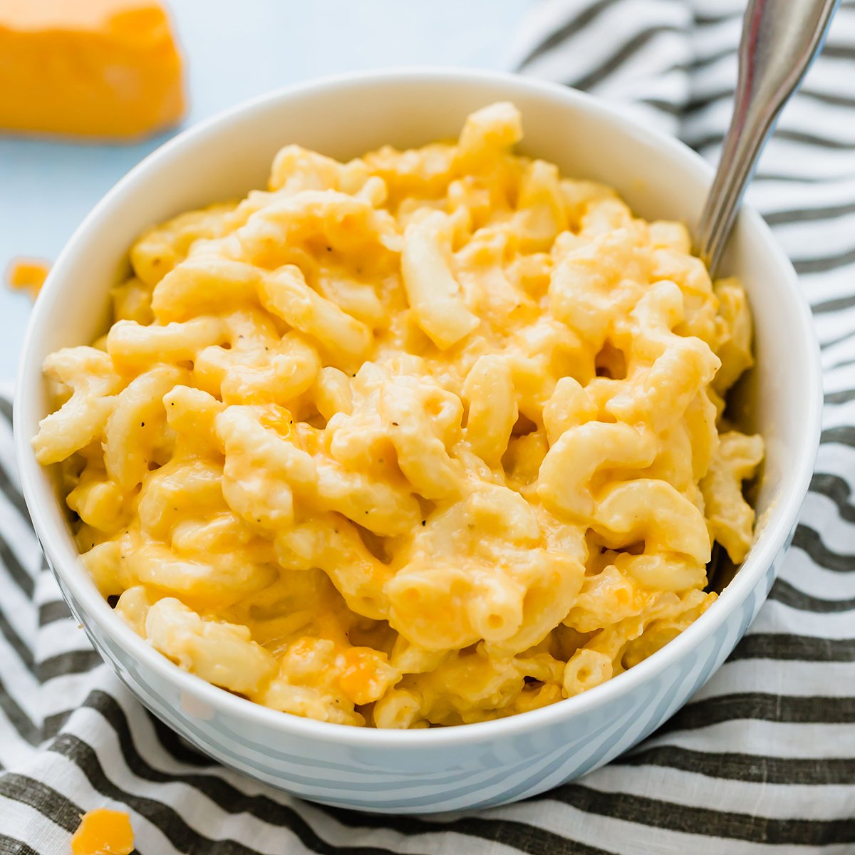Crock pot mac and cheese in a white bowl with a spoon on top of a black and white striped linen.