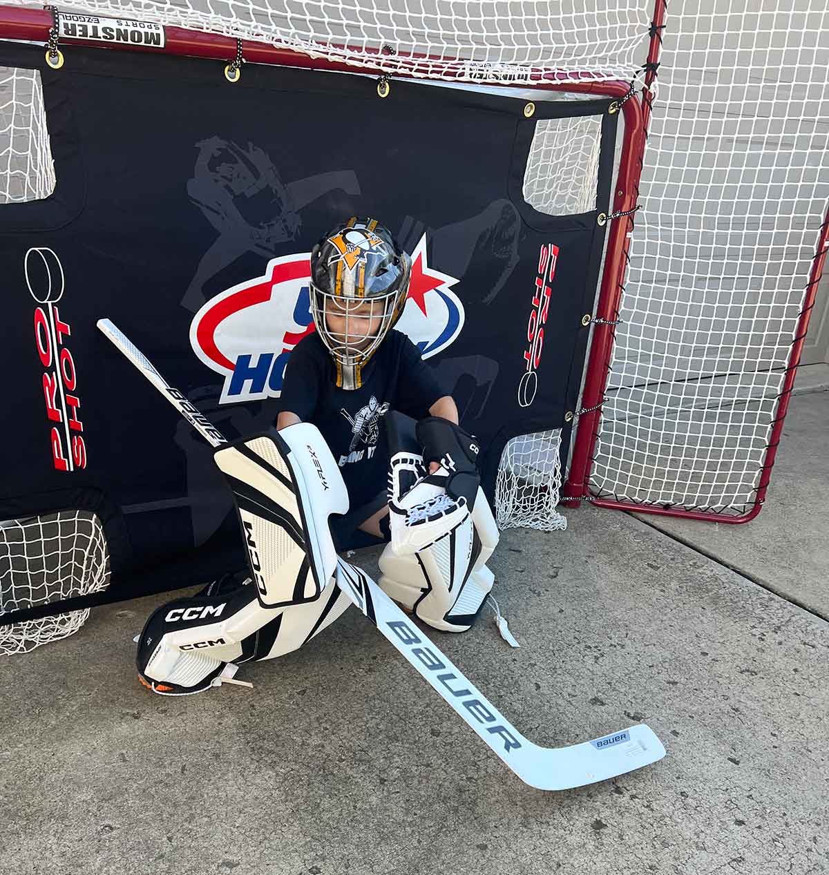 Boy in hockey goalie equipment in front of a net in a driveway.