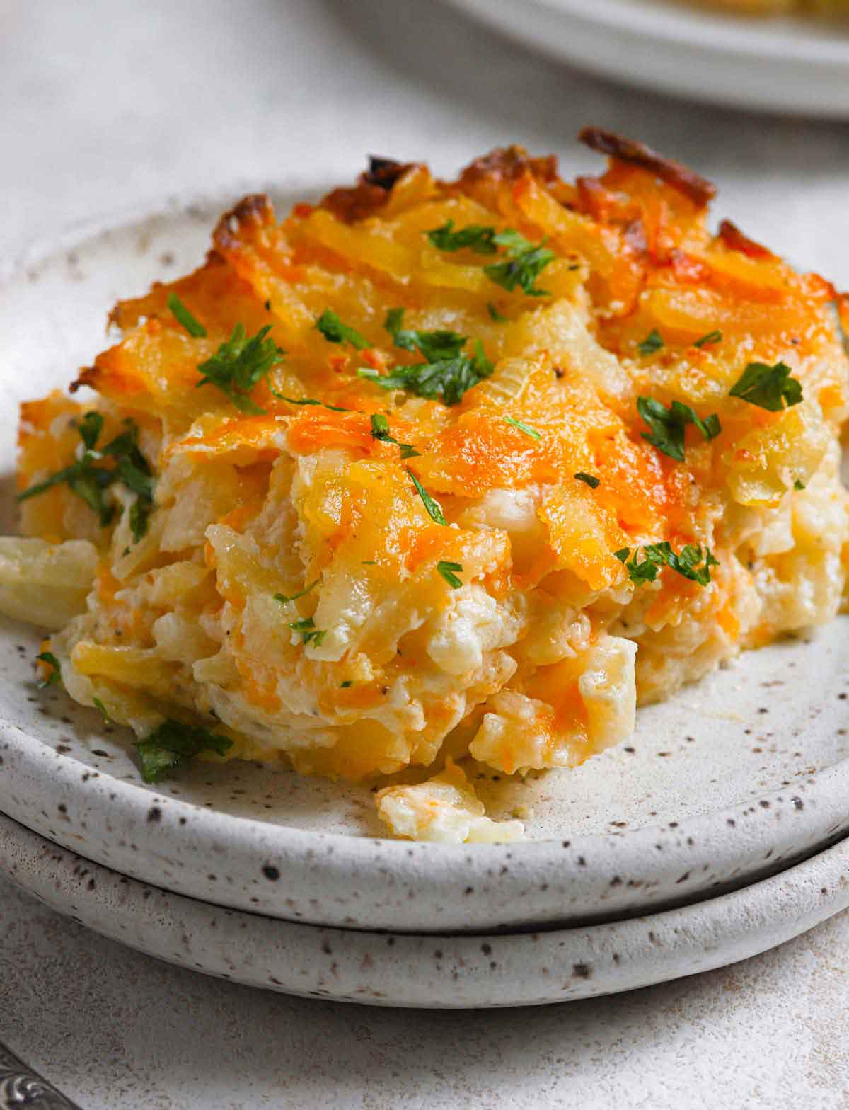 Close up photo of serving of hashbrown casserole on black and white speckled plate.