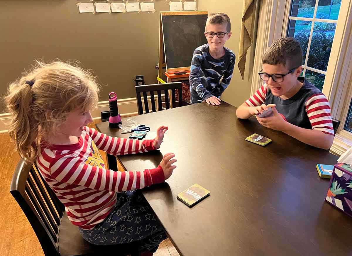 Three children around a small table playing a card game.