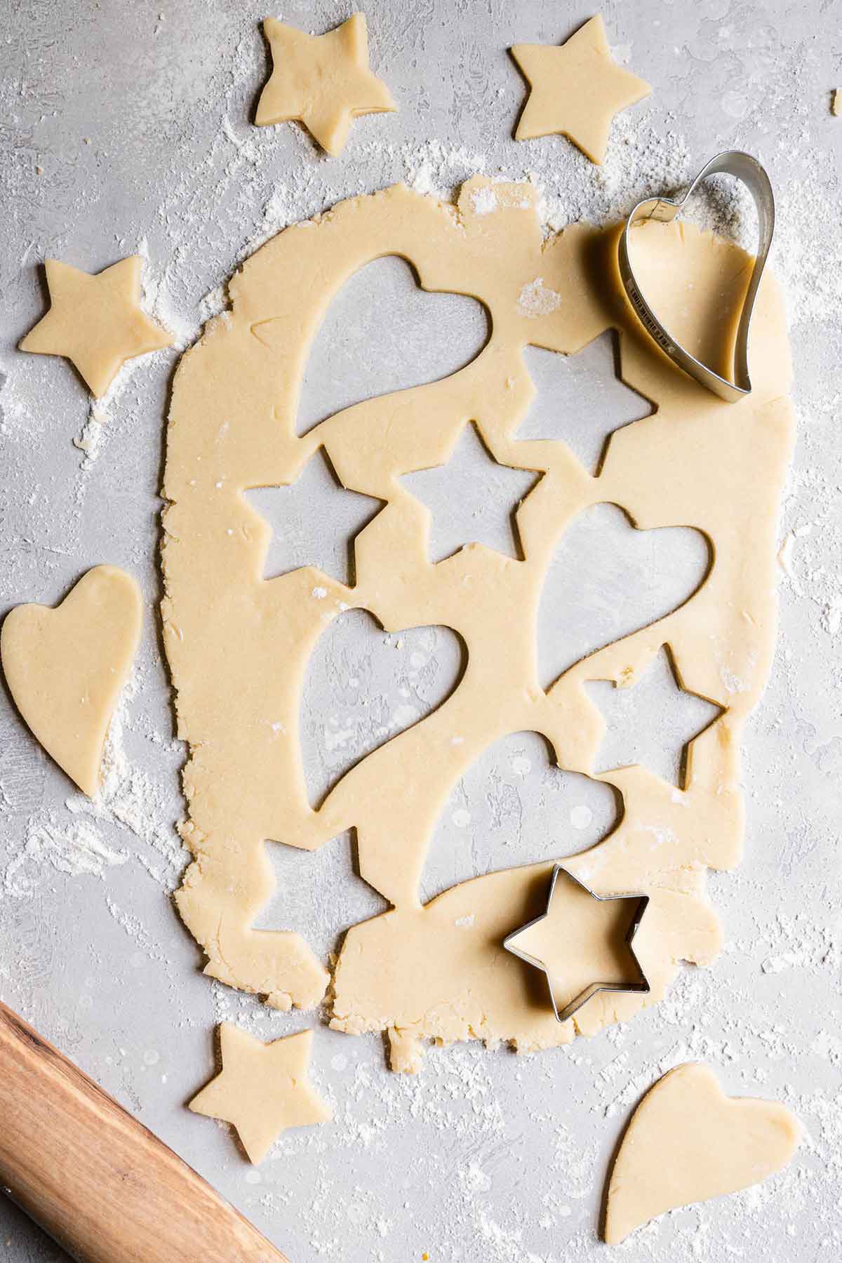 Sugar cookie dough rolled out with hearts and star shapes cut out with cookie cutters.
