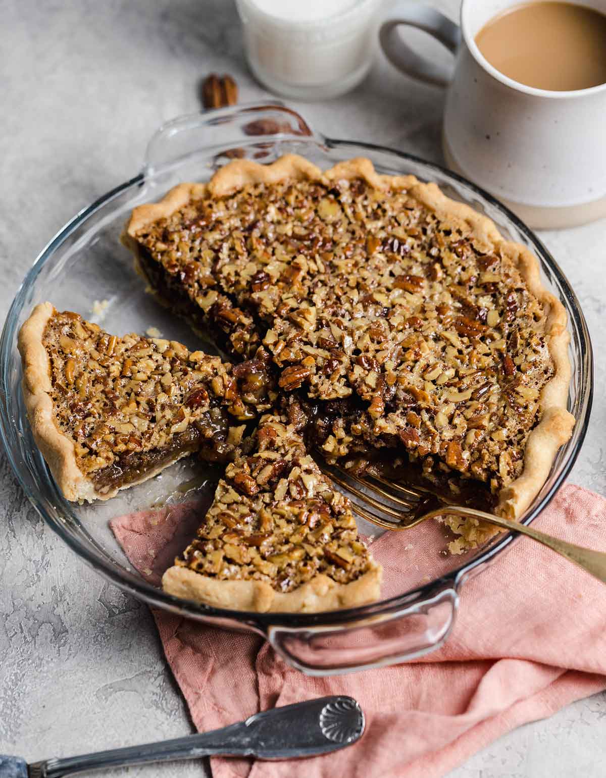 Glass pie plate with pecan pie, two slices cut but still in pie plate with a fork.