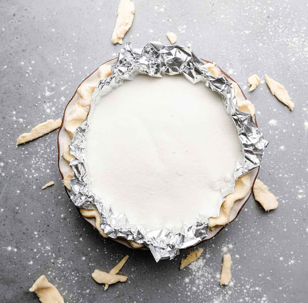 Pie plate lined with pie dough and covered in aluminum foil and filled with sugar.