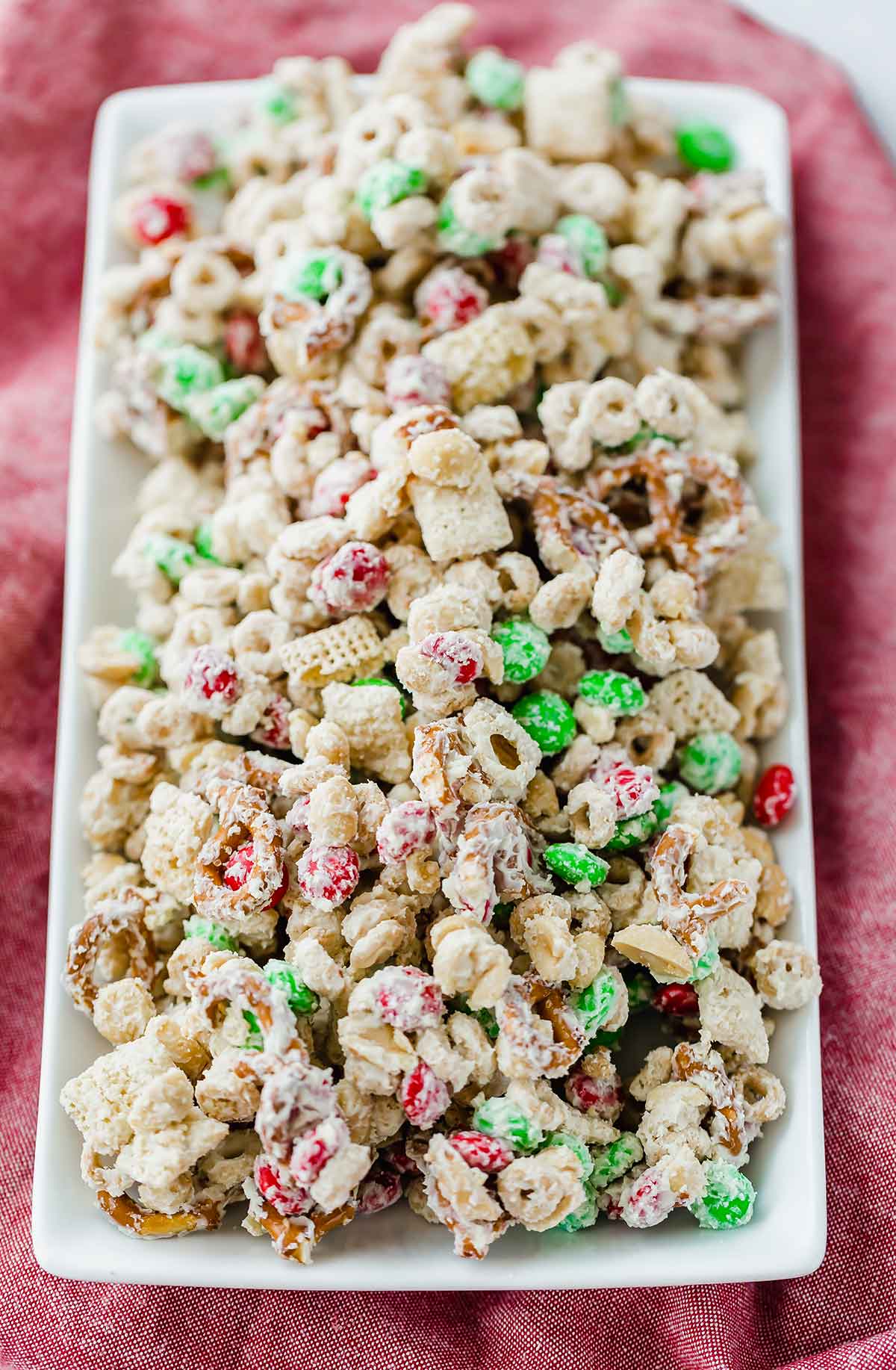 A white tray set on a red background with reindeer chow snack mix on it.