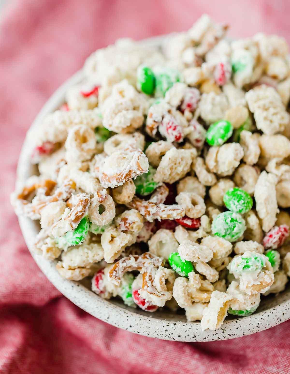 A black and white speckled bowl filled with reindeer chow, set on a red linen background.