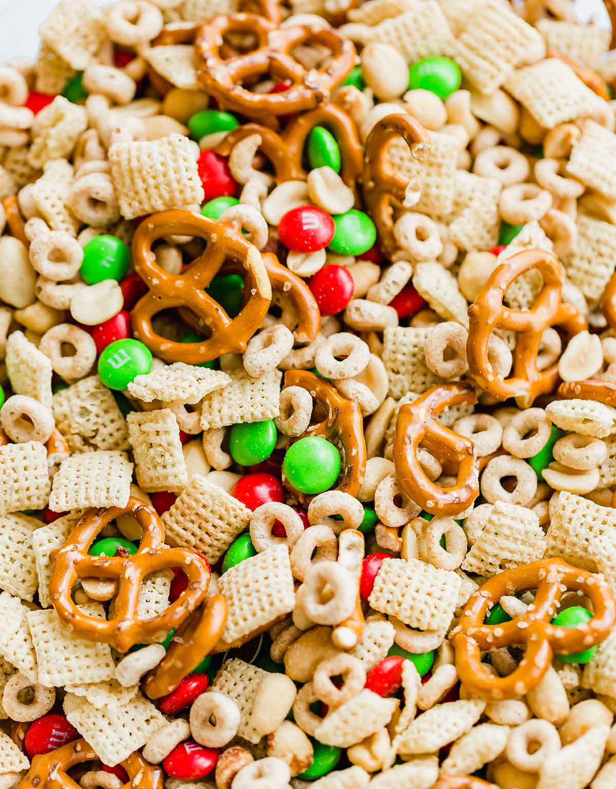 Closeup photo of ingredients for reindeer chow in a bowl - Rice Chex, Cheerios, peanuts, pretzels, and M&Ms.