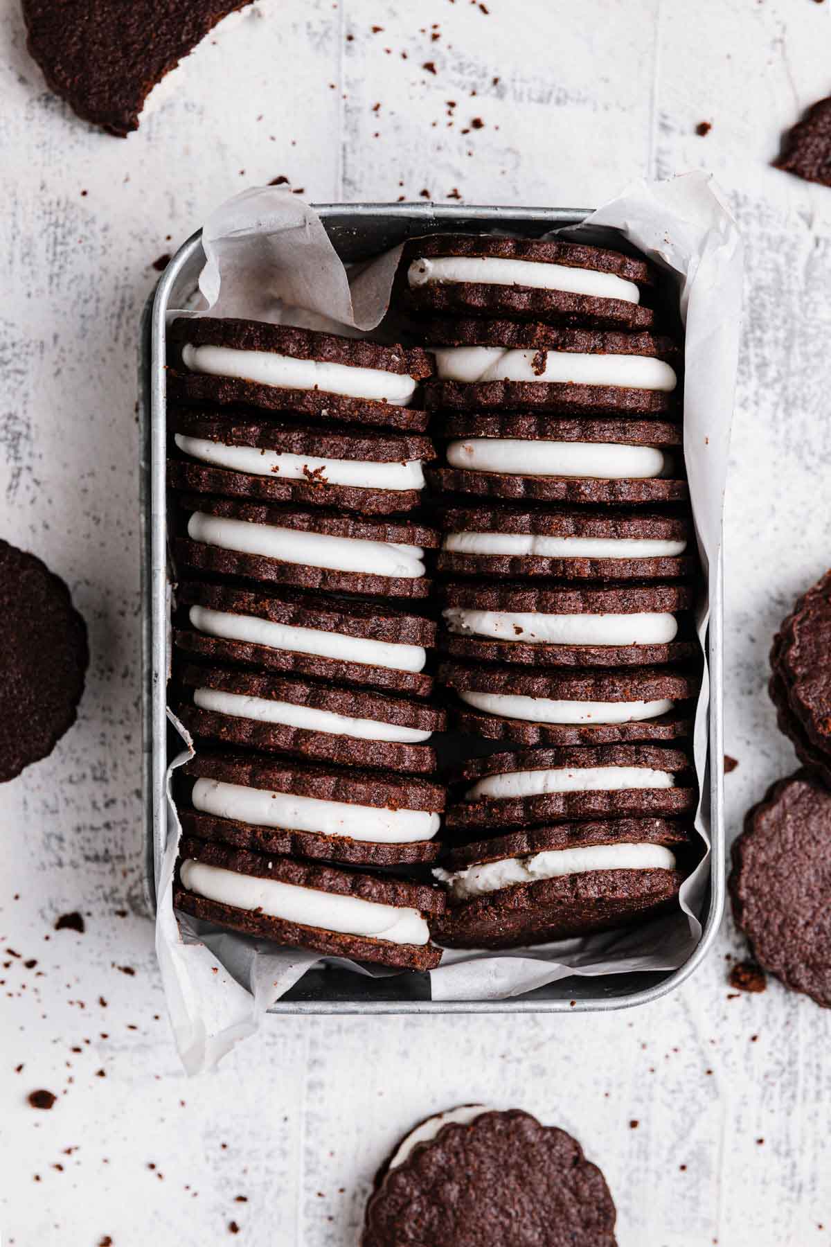 Overhead photo of a tin holding homemade Oreo cookies stacked neatly inside, filling side up.