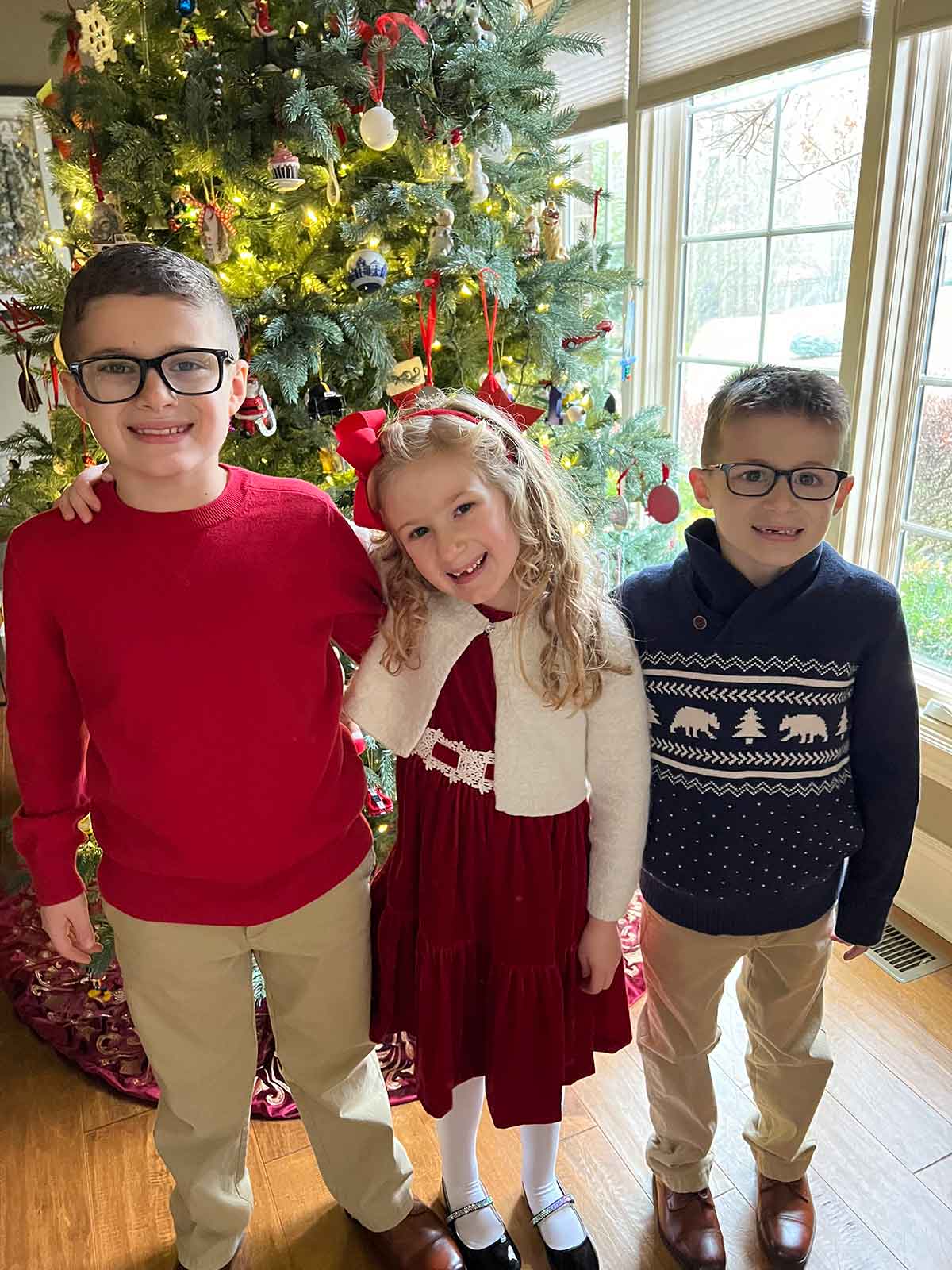 Three children standing in front of a lit Christmas tree.