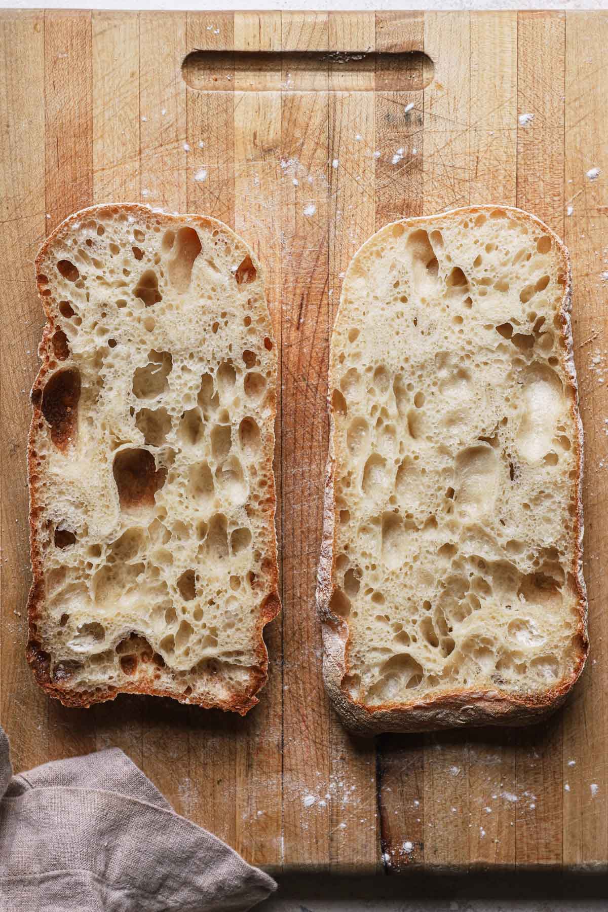 A loaf of baked ciabatta bread slized in half horizontally and both halves laid out cut-side-up on a cutting board.