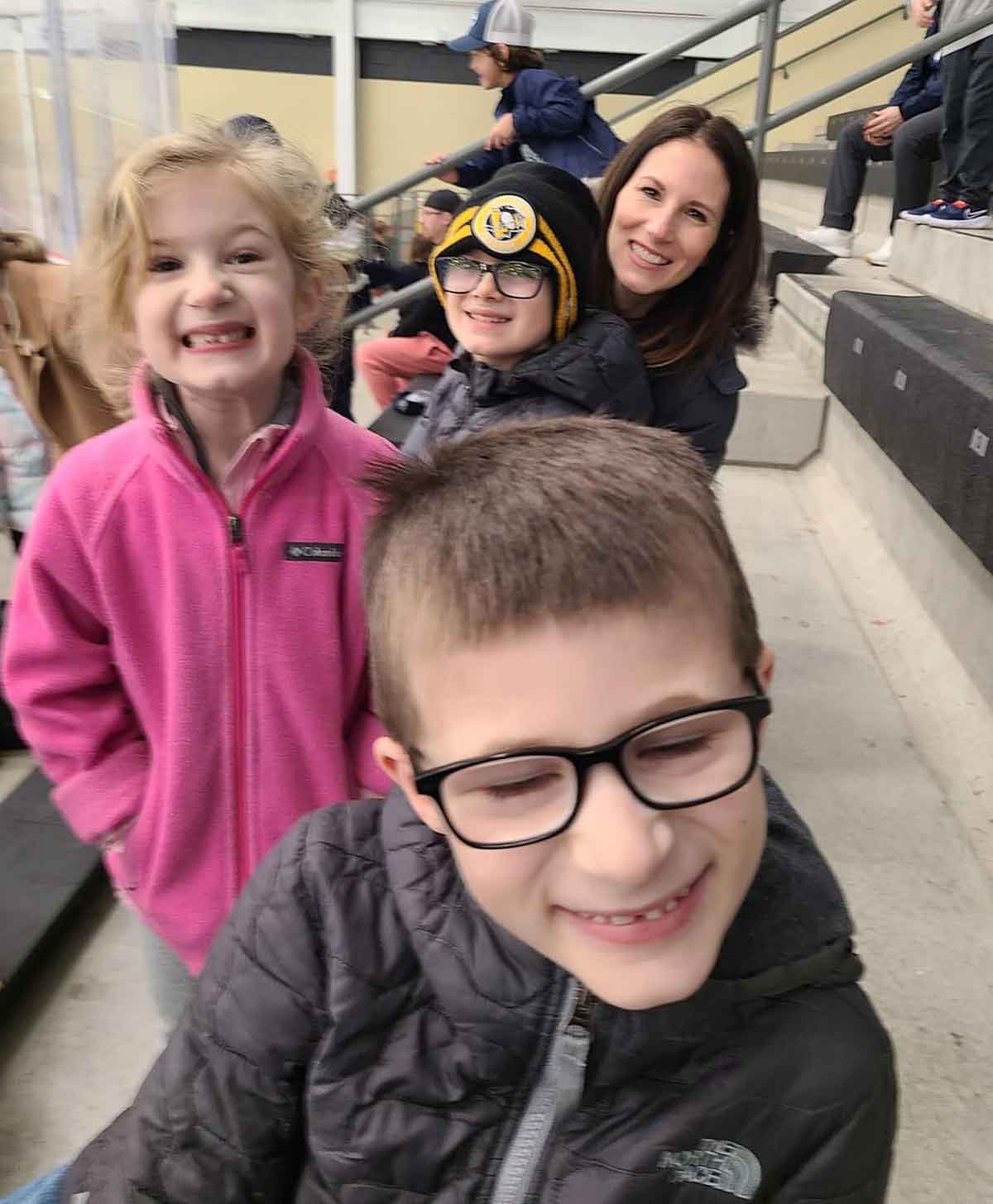 Mom with three kids (two boys and one girl) sitting on bleachers.